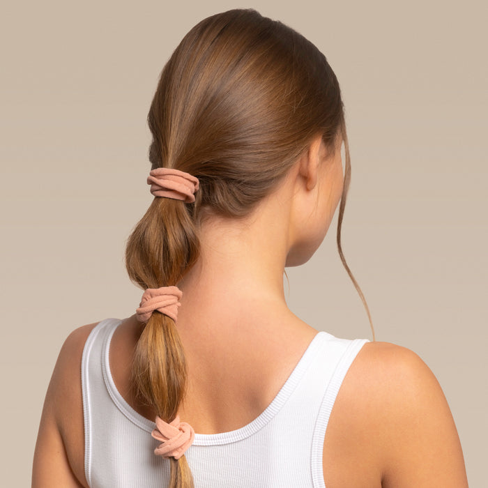 Woman with a bubble ponytail with 3 kitsch petal hair elastics wearing a white tank top against a beige background
