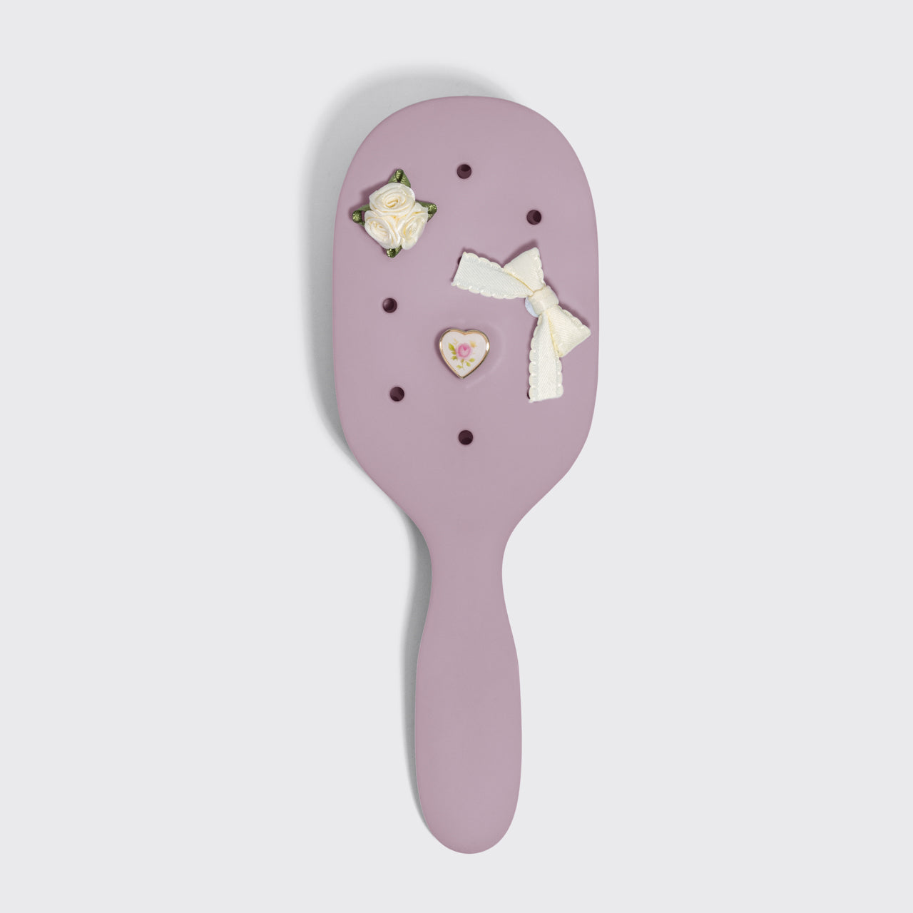 Purple hairbrush with decorative items on a light gray background
