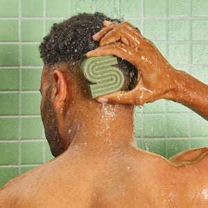 Person applying KITSCH Tea Tree & Mint Clarifying Solid Shampoo Bar directly to wet scalp in shower against green tile — sulfate-free clarifying shampoo bar that detoxes buildup, reduces oiliness, and balances scalp microbiome with Dandrilys® and tea tree & mint blend