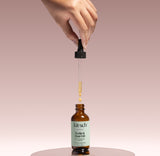 KITSCH Strengthening Rosemary & Biotin Scalp & Hair Oil — product shot — dropper releasing oil into the amber glass bottle on a blush pedestal — 100% plant-based blend of rosemary, jojoba, argan and castor oils with biotin