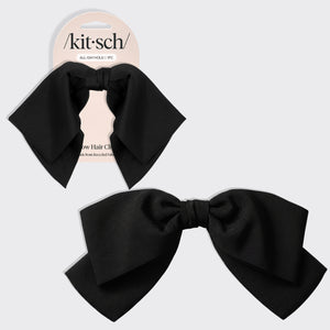 A black bow hair clip shown both on its retail backing card and as a loose product shot, on a light gray background. The brand name 'kitsch' is visible on the card.